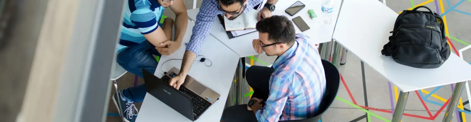 Three men collaborating over a laptop in a modern, geometric-themed office space.